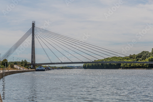 Lanaye cable-stayed bridge, which crosses the Albert Canal with boats anchored below and with green vegetation in the background, cloudy day in Belgium