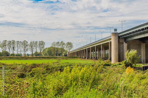 Road bridge A76 (Scharbergbrug) over the Maas river field with green grass and trees, sunny day with blue sky and abundant white clouds in Elsloo and Meers, South-Limburg in the Netherlands Holland