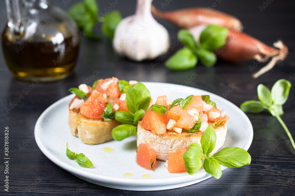 Bruschetta on a white plate with basil, onion, garlic and olive oil in the background Bruschetta on a white plate with basil, onion, garlic and olive oil in the background