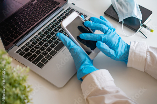 a girl in blue gloves holds a mobile phone in her hand, a laptop stands nearby