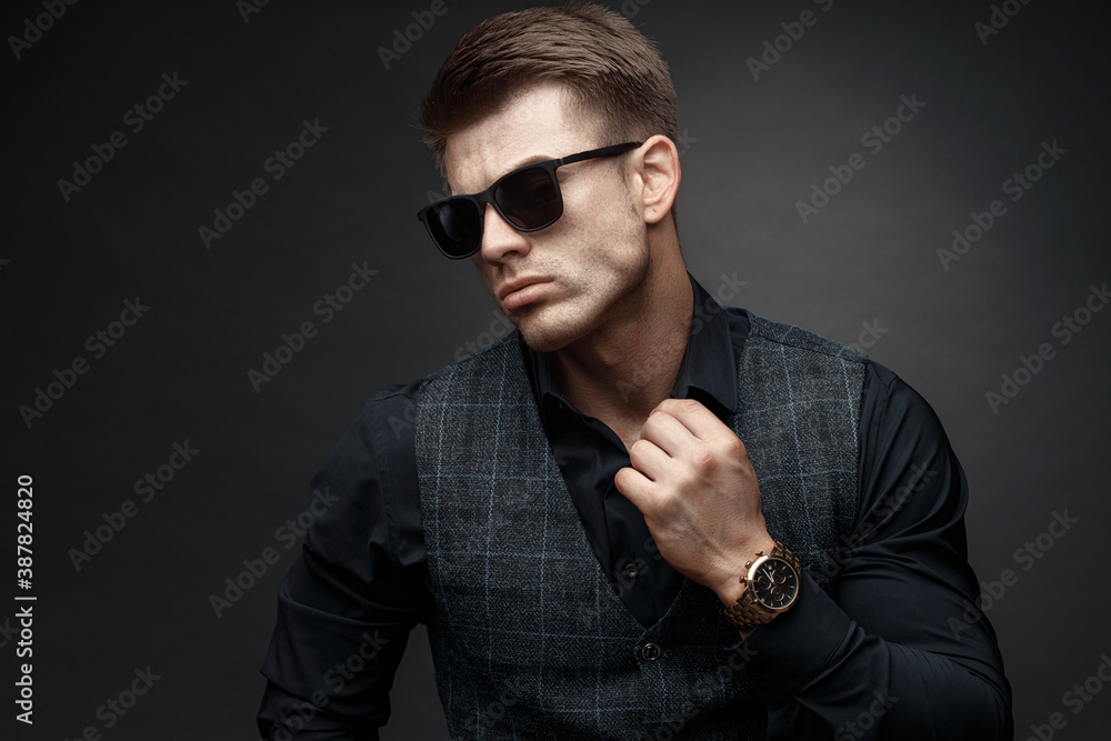 Portrait of beautyful guy on dark background. High fashion model posing in studio. Attractive man in classic suit and sunglasses.