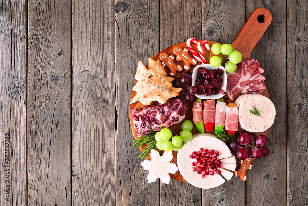 Christmas theme charcuterie board. Overhead view against a dark wood background. Mixed cheese and meat appetizers. - obrazy, fototapety, plakaty 