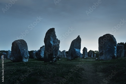 Ancient menhir granite stones at night, close-up. Clear sky, stars, moonlight. Carnac, France. Atmospheric landscape. Travel destinations, tourism, national landmark, sightseeing. culture, history