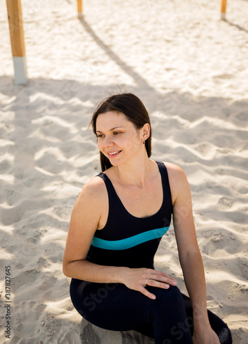 portrait of a happy yoga woman sitting on a sandy beach and looking away