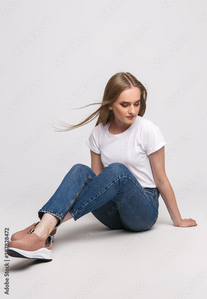 young beautiful woman in a white t-shirt and jeans on a white background. Young woman sit on white background. Photo concept for advertisements of clothes and shoes young beautiful woman in a white t-shirt and jeans on a white background. Young woman sit on white background. Photo concept for advertisements of clothes and shoes