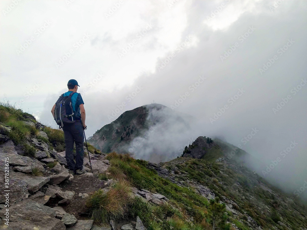 Man with a hat and a backpack on the top of mountain surrounded by fog and clouds