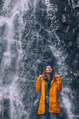 woman in yellow raincoat at autumn waterfall