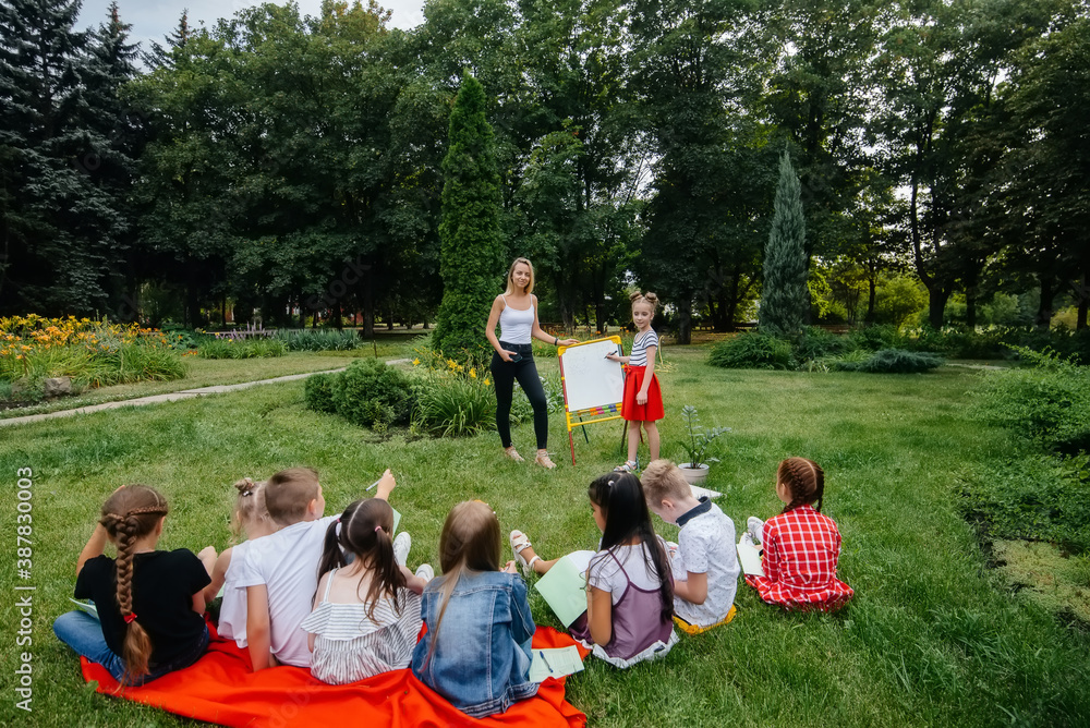 Obraz premium A teacher teaches a class of children in an outdoor Park. Back to school, learning during the pandemic