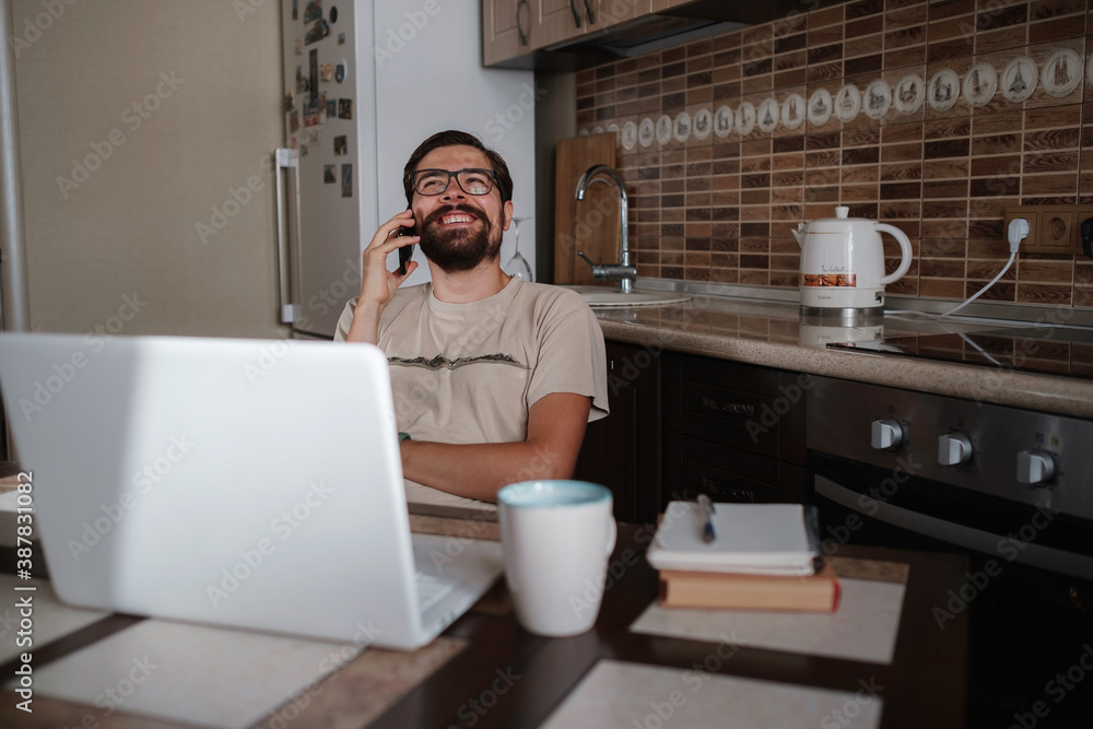 Smiling handsome freelancer working remotely from home. He is speaking on the phone. Smiling handsome freelancer working remotely from home. He is speaking on the phone.