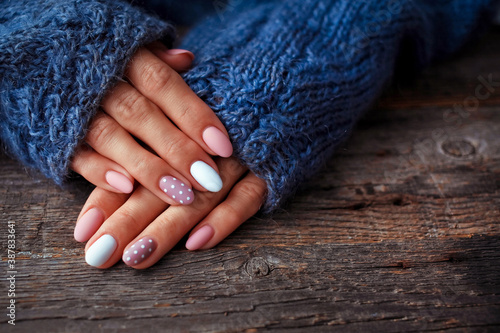 Women is hands with a beautiful manicure, in a knitted sweater on a wooden background in. Autumn trend, polish beige and white polka dots on nails with gel polish, shellac.