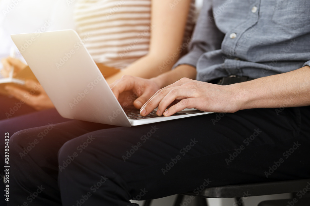 Naklejka premium Group of casual dressed business people working at meeting or conference in sunny office, close-up of hands. Businessman using laptop computer