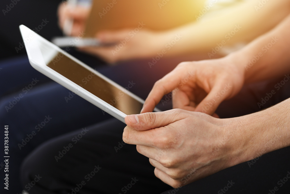 Group of casual dressed business people working at meeting or conference in sunny office, close-up of hands. Businessman using tablet computer