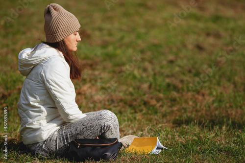 Brunette woman wearing hat sitting on the grass with eyes closed in the park on a beautiful sunny autumn day. Relaxing after hard day. Meditation