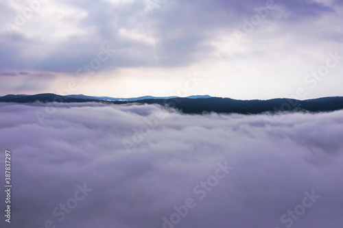Aerial photo above fog. Beautiful sunrise through clouds. Hill tops in distance.