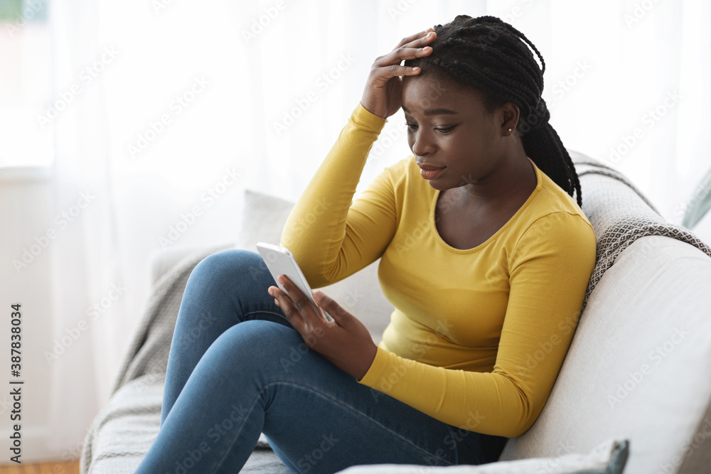 Fototapeta premium Worry African American Female Looking At Smartphone Screen At Home, Reading Message
