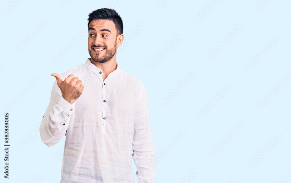 Young handsome man wearing casual clothes smiling with happy face looking and pointing to the side with thumb up. Young handsome man wearing casual clothes smiling with happy face looking and pointing to the side with thumb up.