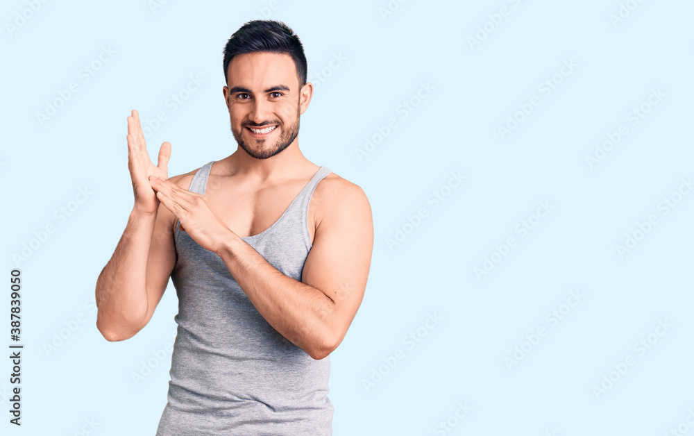 Young handsome man wearing swimwear and sleeveless t-shirt clapping and applauding happy and joyful, smiling proud hands together Young handsome man wearing swimwear and sleeveless t-shirt clapping and applauding happy and joyful, smiling proud hands together