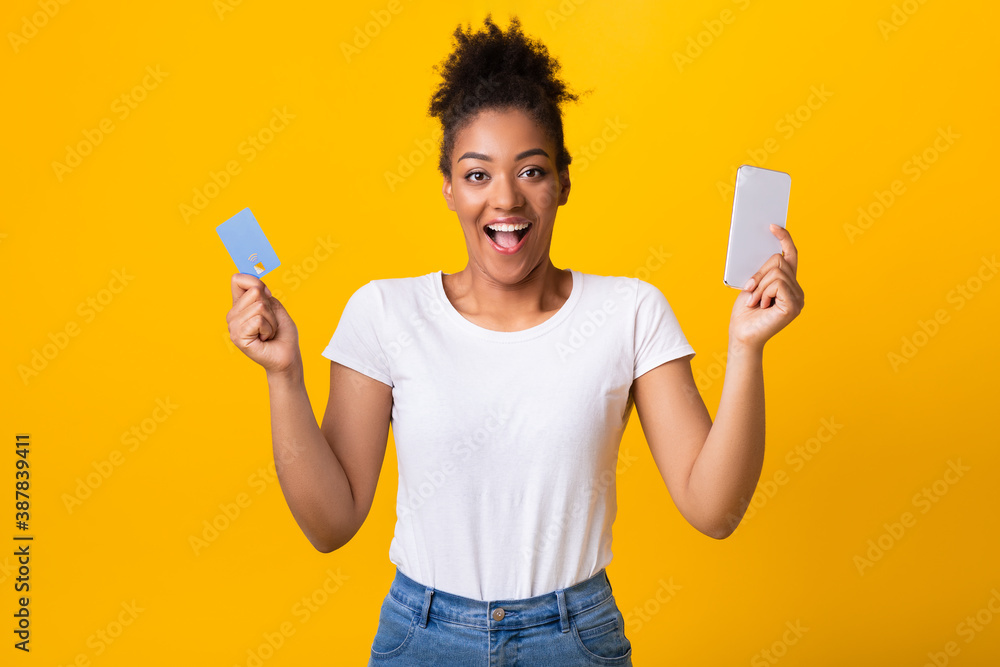 Excited black lady holding credit card and cellphone at studio Excited black lady holding credit card and cellphone at studio