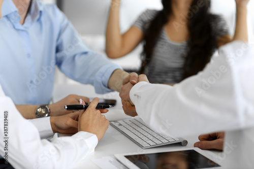 Two businessmen are shaking hands in office while sitting at the desk, close-up. Colleagues applauding of success meeting end. Business people concept