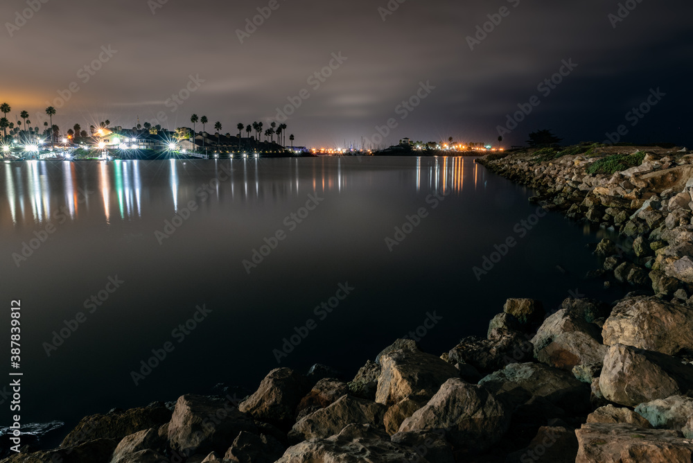 Ventura Marina waters reflecting harbor lamps in the ocean surface as boulder rocks along the shore show changes in tide.