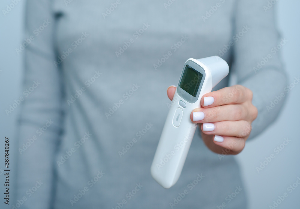 Fototapeta premium Woman holding non-contact digital thermometer in hand on gray background