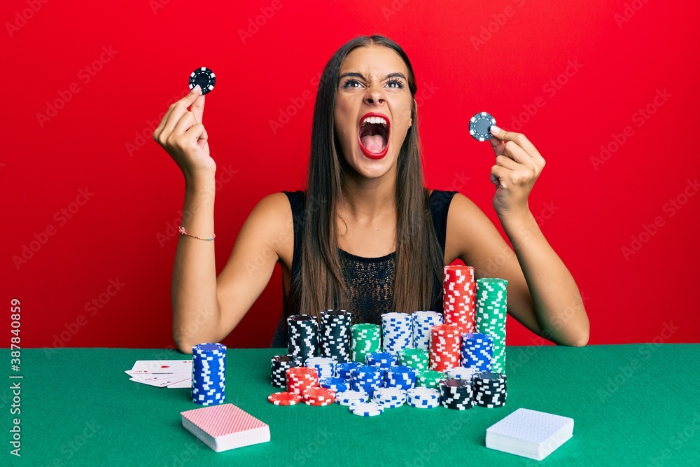 Young hispanic woman sitting on the table holding casino chips angry and mad screaming frustrated and furious, shouting with anger looking up. Young hispanic woman sitting on the table holding casino chips angry and mad screaming frustrated and furious, shouting with anger looking up.