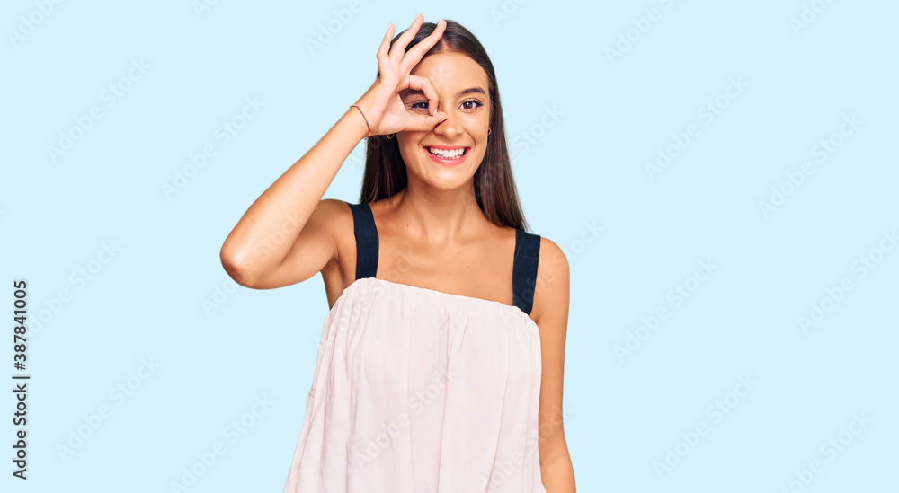 Young hispanic woman wearing casual clothes doing ok gesture with hand smiling, eye looking through fingers with happy face. Young hispanic woman wearing casual clothes doing ok gesture with hand smiling, eye looking through fingers with happy face.