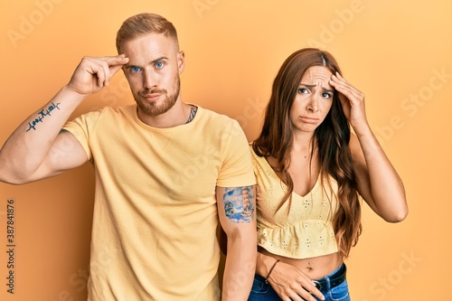 Young couple of girlfriend and boyfriend hugging and standing together worried and stressed about a problem with hand on forehead, nervous and anxious for crisis