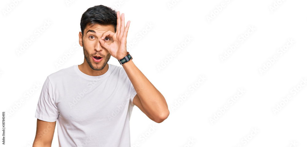 Young handsome man wearing casual white tshirt doing ok gesture shocked with surprised face, eye looking through fingers. unbelieving expression. Young handsome man wearing casual white tshirt doing ok gesture shocked with surprised face, eye looking through fingers. unbelieving expression.