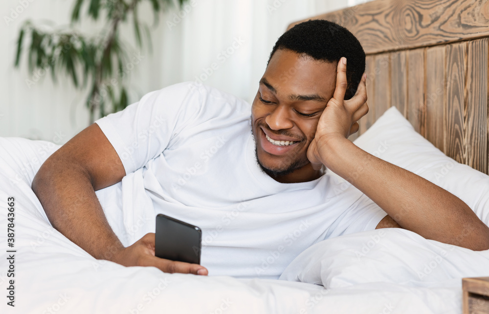 African Man With Smartphone Using Mobile App Lying In Bed African Man With Smartphone Using Mobile App Lying In Bed