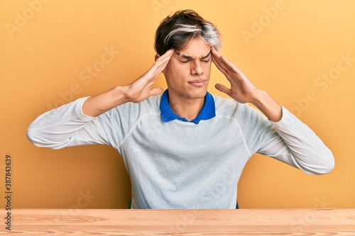 Young hispanic man wearing casual clothes sitting on the table with hand on head, headache because stress. suffering migraine.