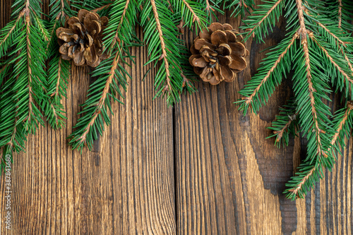 Fir, spruce branches, pine cones on brown wooden background with copy space