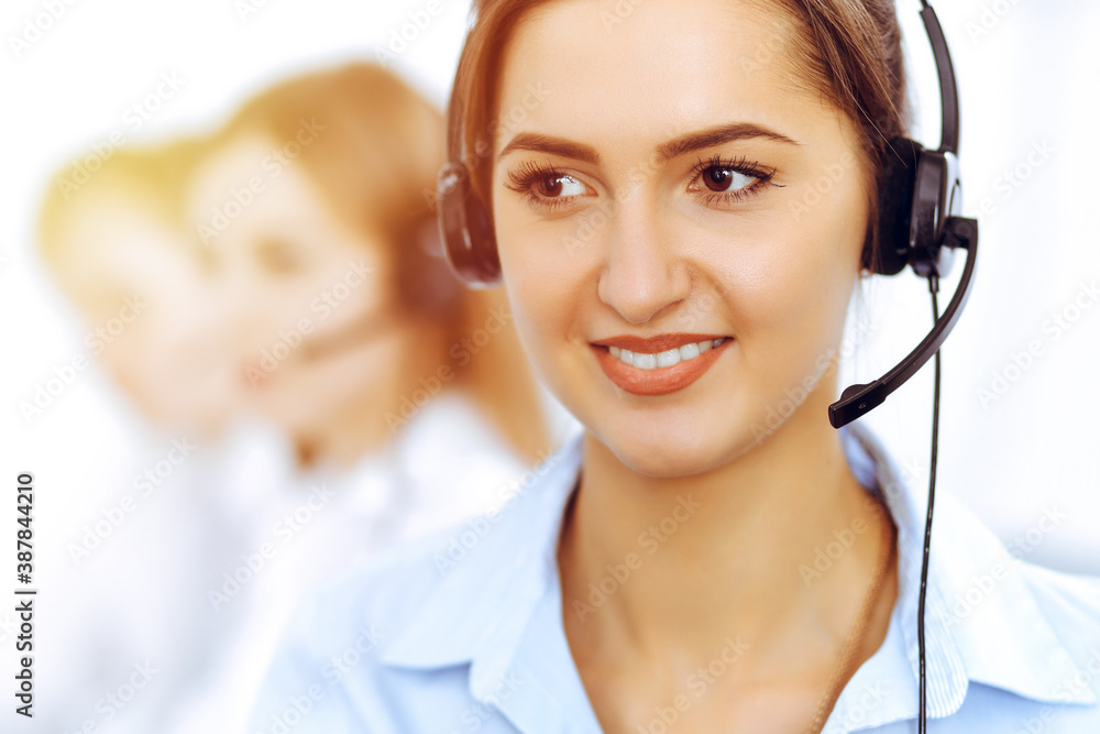 Call center operators. Focus on beautiful business woman using headset in sunny office Call center operators. Focus on beautiful business woman using headset in sunny office