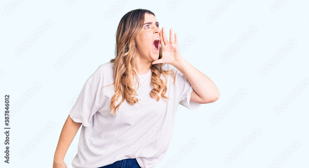 Young caucasian woman wearing casual clothes shouting and screaming loud to side with hand on mouth. communication concept. Young caucasian woman wearing casual clothes shouting and screaming loud to side with hand on mouth. communication concept.