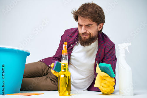 A man lies on the floor with a bucket of detergents providing services light background