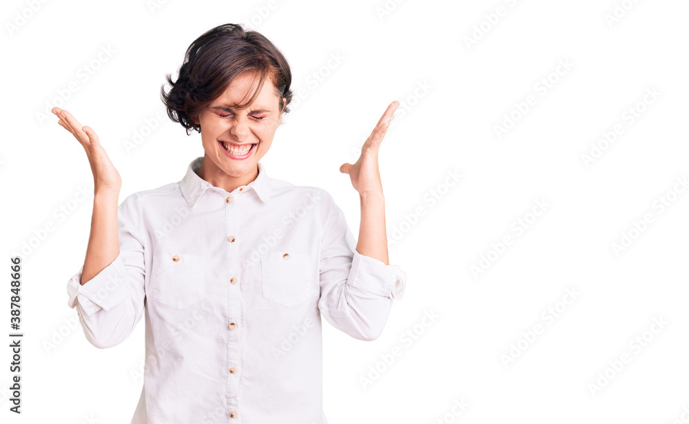 Beautiful young woman with short hair wearing elegant white shirt celebrating mad and crazy for success with arms raised and closed eyes screaming excited. winner concept Beautiful young woman with short hair wearing elegant white shirt celebrating mad and crazy for success with arms raised and closed eyes screaming excited. winner concept