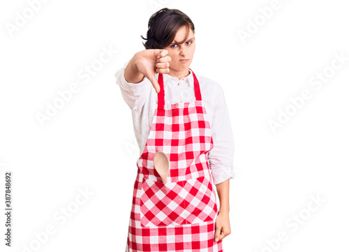 Beautiful young woman with short hair wearing professional cook apron looking unhappy and angry showing rejection and negative with thumbs down gesture. bad expression.