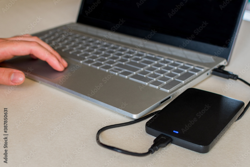 External hard drive connect to laptop computer on desk. A portable hard drive. The concept of data storage.