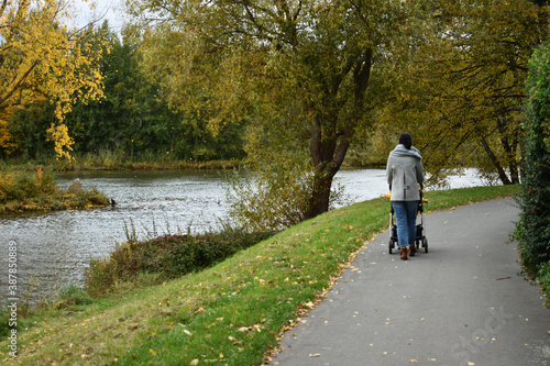 a woman lady with baby stroller buggy walking near river Weser in autumn spring fall in Nienburg Germany