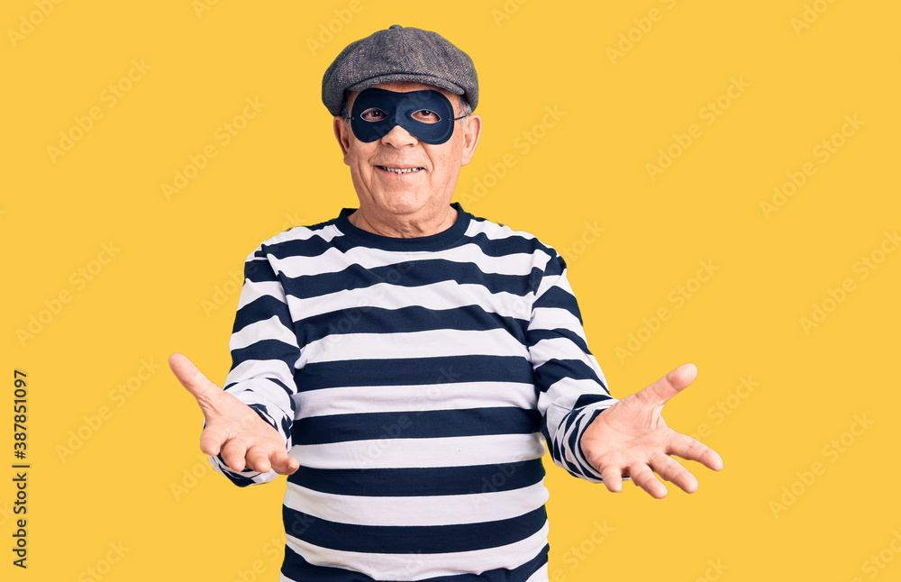 Fototapeta premium Senior handsome man wearing burglar mask and t-shirt smiling cheerful offering hands giving assistance and acceptance.
