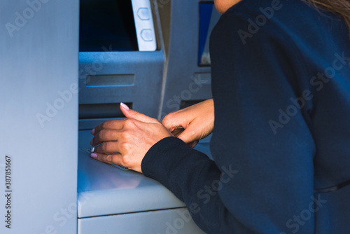 Woman cover with free hand and hide the keypad with PIN number when withdraw cash money at an ATM machine. ATM safety and security measures. Protect your PIN