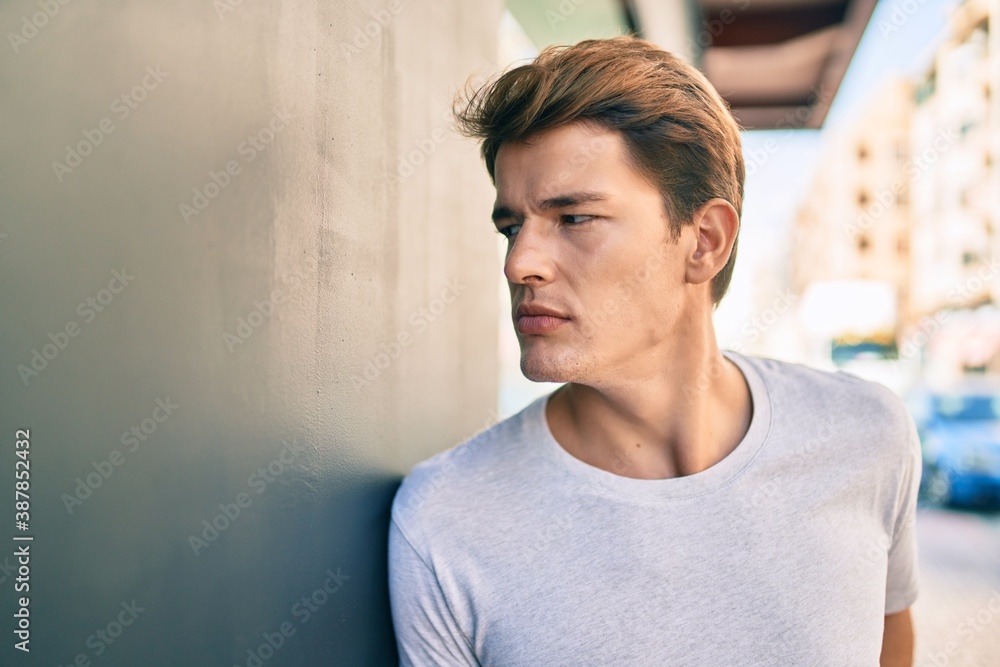 Fototapeta premium Young caucasian man with serious expression leaning on the wall at the city.