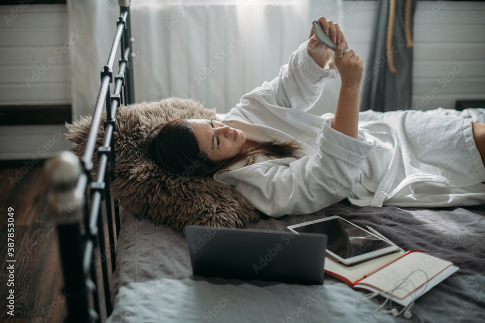 A woman is resting on a bed in a bedroom with a telephone