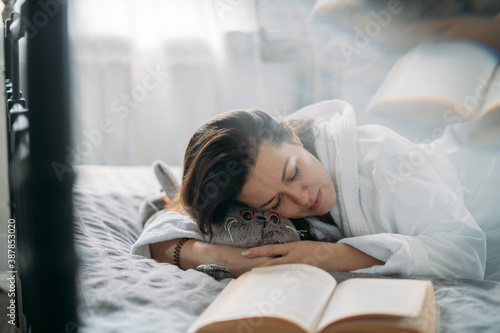 A woman in a bathrobe sleeps on a bed with a book