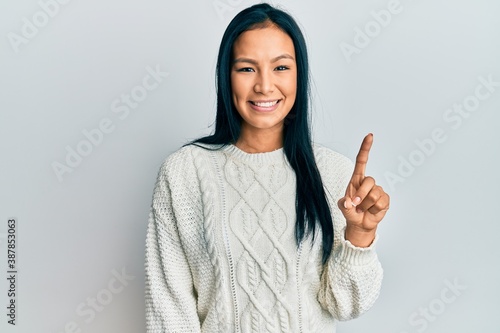 Beautiful hispanic woman wearing casual winter sweater over white background smiling with an idea or question pointing finger up with happy face  number one