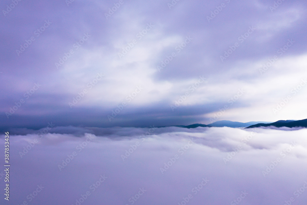 Aerial photo above fog. Beautiful sunrise through clouds. Hill tops in distance.