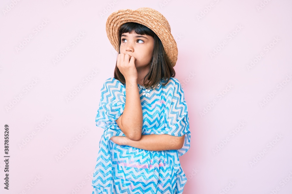 Young little girl with bang wearing summer dress and hat looking stressed and nervous with hands on mouth biting nails. anxiety problem. Young little girl with bang wearing summer dress and hat looking stressed and nervous with hands on mouth biting nails. anxiety problem.