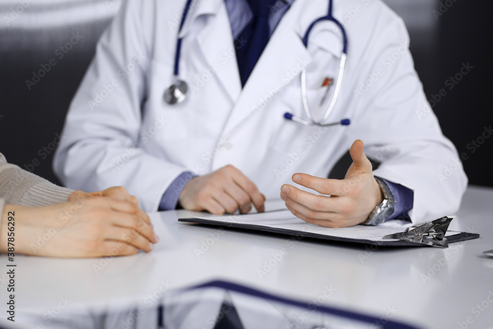 Unknown male doctor and patient woman discussing something while sitting in clinic. Best medical service in hospital, medicine, pandemic stop Unknown male doctor and patient woman discussing something while sitting in clinic. Best medical service in hospital, medicine, pandemic stop