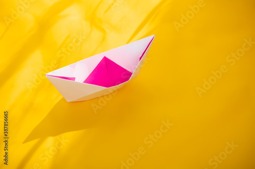 Pink origami boat against the yellow background