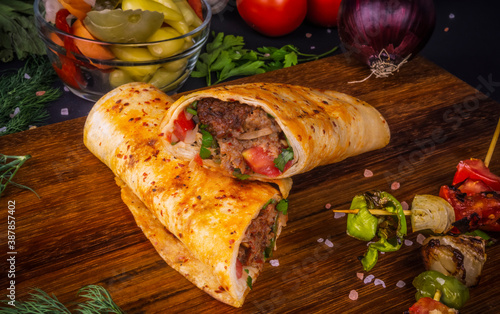 Turkish and Arabic Traditional Ramadan Adana Kebab Roll Wrap serving with yogurt  aubergine salad and hot pepper pickles on rustic wooden background.